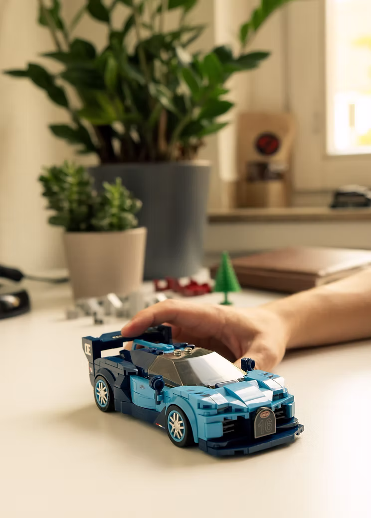 Hand platziert ein gebautes Klemmbaustein-Auto auf einem Schreibtisch